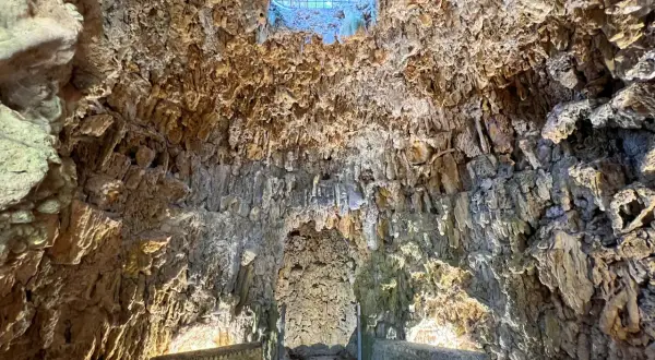 Interno di una grotta con stalattiti e stalagmiti, illuminata da una luce soffusa che filtra da un'apertura in alto. Sembra il ventre del **colosso dell'Appennino**.
