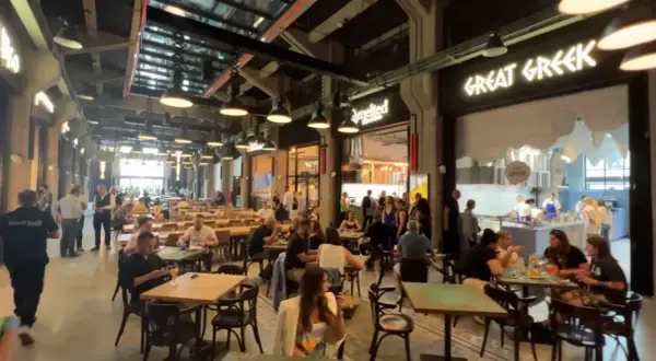 Tętniący życiem food hall w Gdańsku. Ludzie siedzą przy stołach, jedzą i rozmawiają. W tle widać lokal "Great Greek".