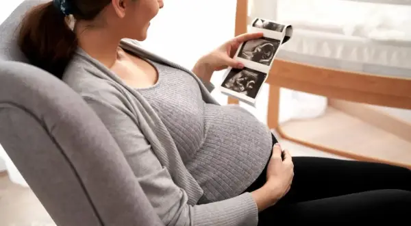 Ciężarna kobieta z uśmiechem ogląda zdjęcia z usg wątroby swojego dziecka.