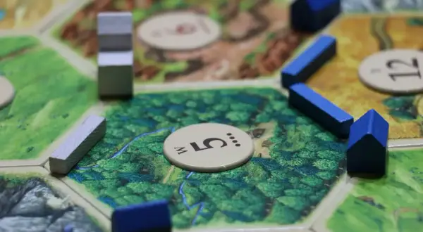 Drewniane domki i drogi na planszy do gry strategicznej. Gracze budują osady, by zdobyć surowce i rozwijać swoje imperium.