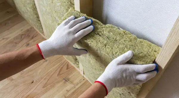Mani guantate posizionano materiale isolante per un cappotto interno fai da te.