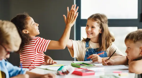 Kinder geben sich beim Lernen die Hand. Sie arbeiten an ihren Aufgaben, was gute Gruppenarbeit Methoden zeigt.