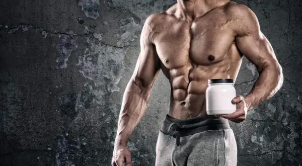 Muscoloso bodybuilder con addominali scolpiti tiene un barattolo bianco, simbolo di un efficace schema integrazione bodybuilding.