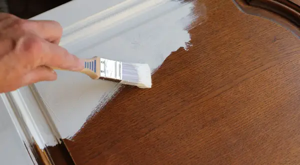 Mano che dipinge con pennello bianco su mobile in legno scuro. La cementite a cosa serve? A preparare la superficie per una finitura perfetta.