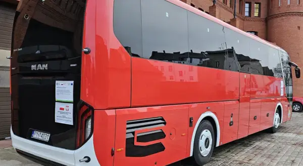 Czerwony autokar MAN Lion's Coach zaparkowany przed ceglanym budynkiem. Może to być przystanek w podróży z Bolesławca do Poznania.