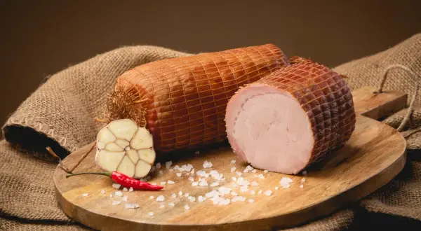 Dwie wędzone szynki na desce, obok czosnek, papryczka chili i sól. Idealne składniki, by dowiedzieć się, jak wędzić szynkę.