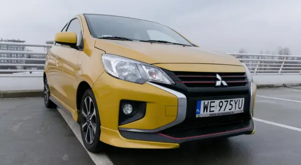 Żółty Mitsubishi Space Star 2004 z czarnym grillem i czerwonymi akcentami stoi na parkingu.