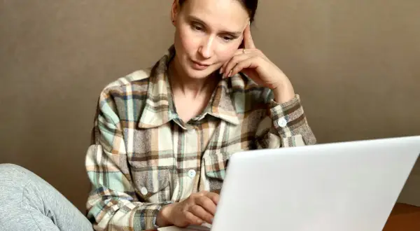 Kobieta zamyślona przy laptopie szuka informacji, jak usunąć negatywny wpis w BIK.