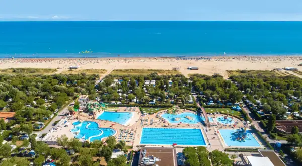 Widok z lotu ptaka na plażę i kompleks basenów w **marina do Venezia**. Widać morze, piaszczystą plażę z leżakami, camping i zjeżdżalnie wodne.