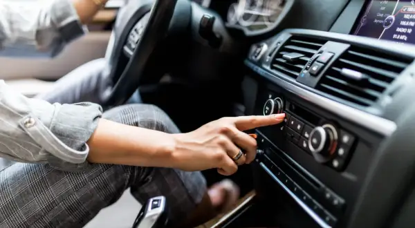 Une main ajuste le volume du radio qui grésille dans la voiture, cherchant la station parfaite pour le trajet.