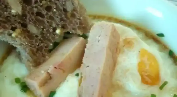 Œuf cocotte au foie gras, servi avec une tranche de pain aux céréales et des herbes fraîches. Un délice pour le palais.