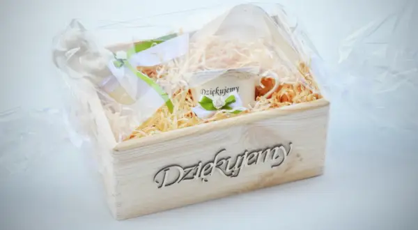 Drewniana skrzynka z napisem "Dziękujemy", wypełniona siankiem, zawiera filiżankę z napisem "Dziękujemy" i ozdobne wstążki. Idealny tekst podziękowania dla księdza.