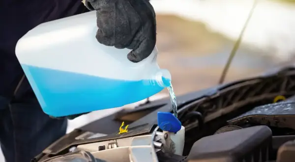 Persona con guantes vierte líquido azul de un bidón en el depósito del limpiaparabrisas. Es lo mismo refrigerante que anticongelante.