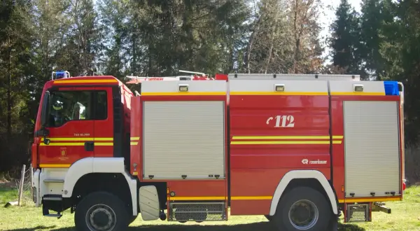 Czerwony wóz strażacki z białymi i żółtymi pasami, numerem 112 i niebieskimi światłami na dachu.