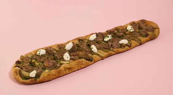 Deliciosa coca de recapte con salchicha, alcachofas y queso de cabra, lista para compartir.