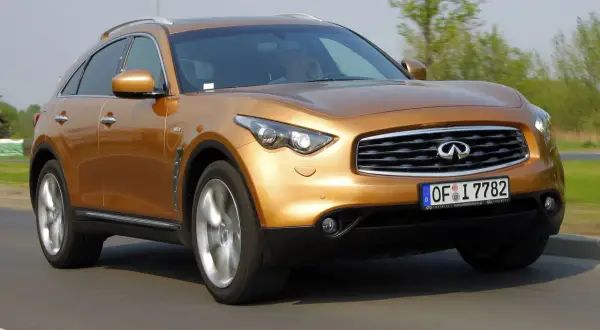 Złoty Infiniti FX35 pędzi po drodze, jego sylwetka jest dynamiczna i sportowa.