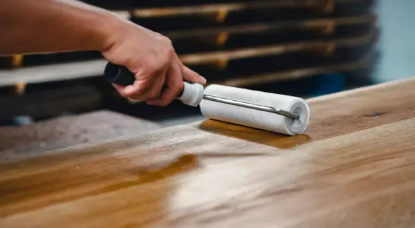 Main d'artisan appliquant un vernis sur un plateau en bois avec un rouleau, étape clé pour savoir comment vitrifier une table en bois.