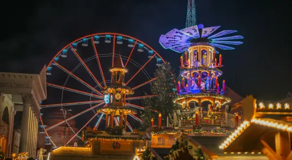 Ein beleuchtetes Riesenrad in Karlsruhe strahlt neben einer Weihnachts-Pyramide.