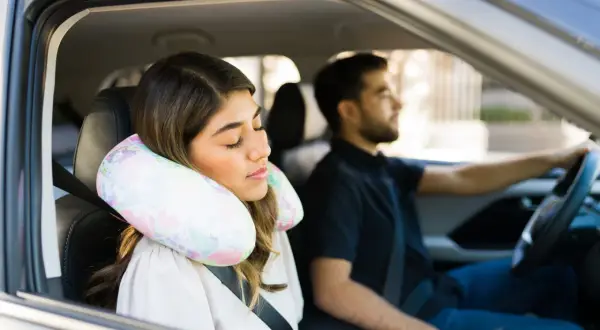 Donna dorme in auto con un cuscino cervicale fai da te, mentre l'uomo guida.