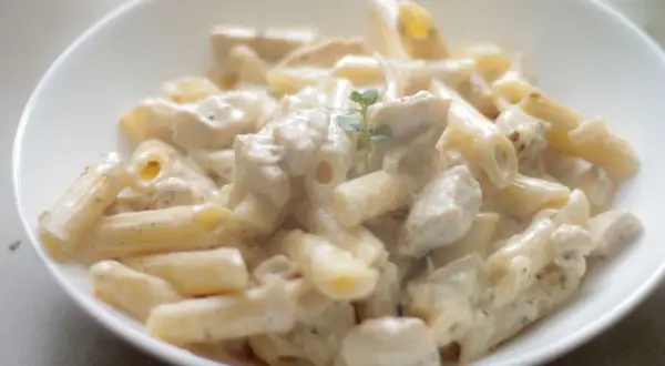 Penne z kurczakiem w kremowym sosie śmietanowo-serowym, udekorowane gałązką ziół. Pyszne danie gotowe do podania.