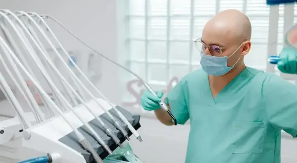 Dentysta w masce i rękawiczkach przygotowuje sprzęt. Zastanawiasz się, ile zarabia dentysta miesięcznie?