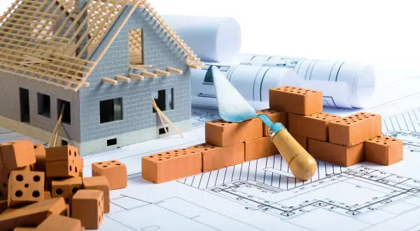 Modello di casa in costruzione su progetti, mattoni e cazzuola. Pianificazione per il rinforzo fondazioni esistenti.