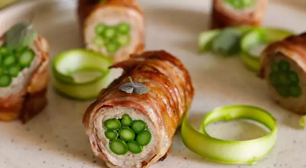Deliziosi involtini di carne con asparagi freschi, avvolti in pancetta croccante e guarniti con erbe aromatiche.