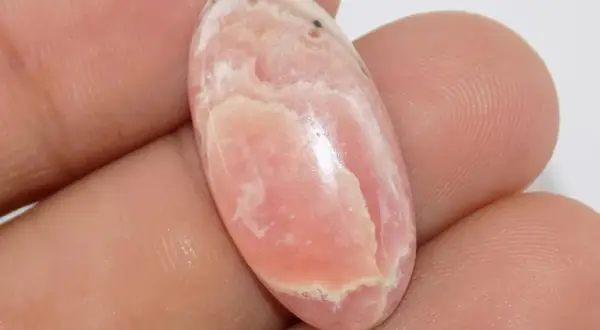 Un óvalo de rodocrosita rosa con vetas blancas, mostrando sus vibrantes propiedades.
