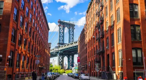 Urokliwe dzielnice Nowego Jorku: Manhattan Bridge wyłaniający się między ceglanymi kamienicami z DUMBO.