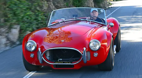 Ein Mann fährt einen roten Shelby Cobra 427 auf einer kurvigen Straße.