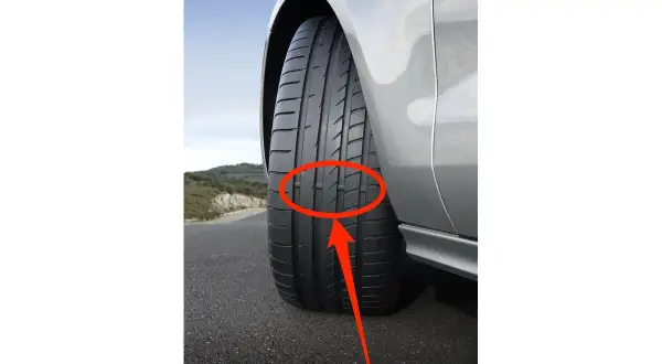 Neumáticos desgastados en un coche plateado en una carretera. La banda de rodadura muestra un desgaste desigual, indicando la necesidad de reemplazo.