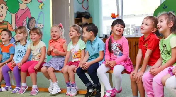 Uśmiechnięte dzieci siedzą w przedszkolu. Widać, ile lat ma się w przedszkolu – to wiek radości i zabawy.