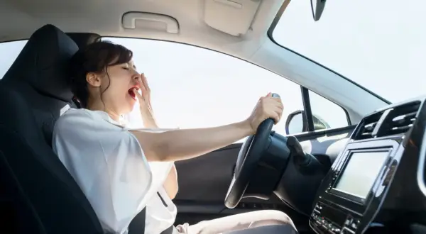 Mujer bostezando al volante. La fatiga puede alterar el tiempo de reacción del conductor, haciendo que el viaje sea peligroso.