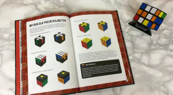 Instrukcja jak krok po kroku ułożyć kostkę Rubika. Książka z ilustracjami pokazuje etapy układania białej ściany, krawędzi i narożników.