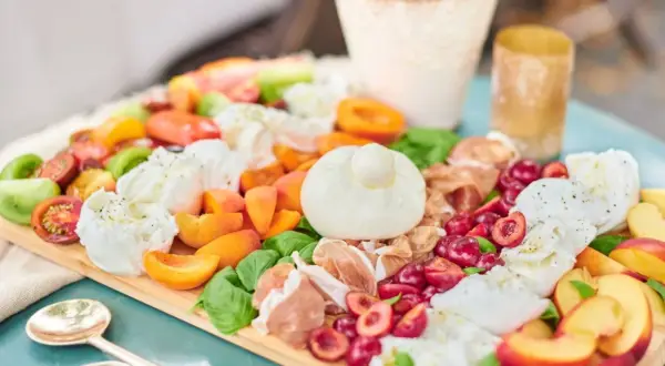 Antipasti-Platte mit Kerze, Wurst, Käse, Oliven und Brot auf Holztisch.