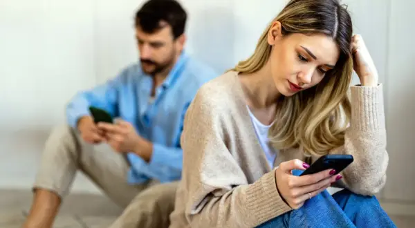 Een vrouw en man zitten apart, beiden op hun telefoon. Ze voelen zich leeg in hun relatie, de afstand tussen hen is voelbaar.