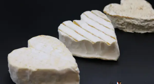 Trois fromages Neufchâtel en forme de cœur, dont un avec des stries, sur fond noir.