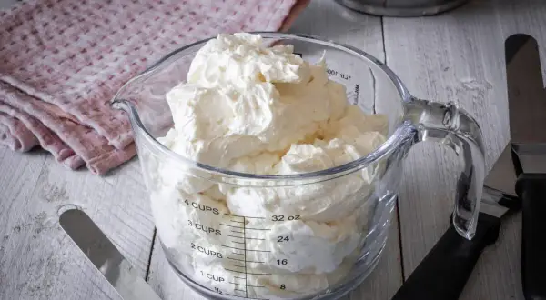 Ein Messbecher gefüllt mit luftiger Swiss Meringue Buttercreme, bereit für süße Kreationen.