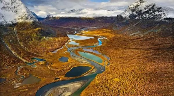 Herbstliche Farben im Tal mit Fluss und Seen, ideal für fernwanderwege schweden. Schneebedeckte Berge im Hintergrund.