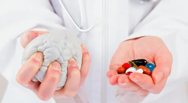 Mains tenant un cerveau en plastique et une poignée de pilules colorées, symbolisant la recherche sur la maladie de Parkinson, dernière découverte.