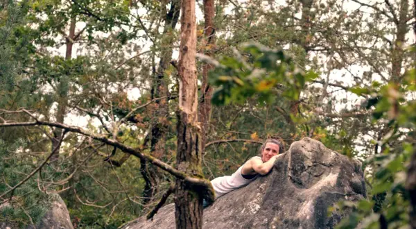Frau ruht auf einem großen Fontainebleau Boulder im Wald, umgeben von Bäumen.