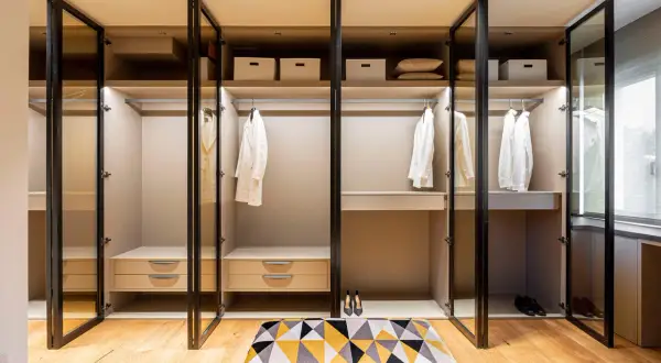 Armario empotrado moderno con puertas de cristal, perchas con ropa blanca y cajones.