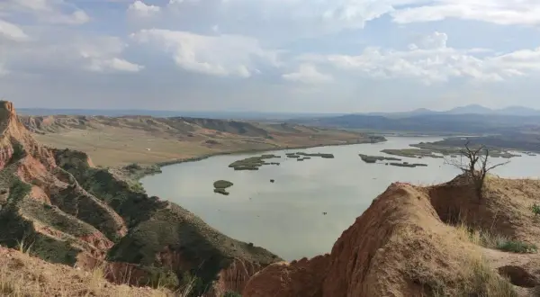 Paisaje de barrancos ocres y un lago sereno, ideal para una ruta de senderismo.