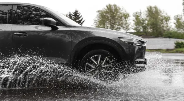 Ciemny samochód na mokrej drodze, koło rozpryskuje wodę, groźny aquaplaning.