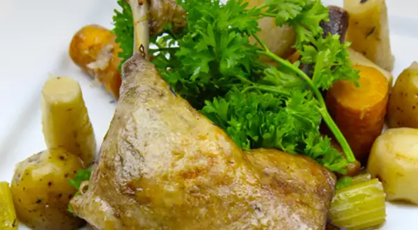 Une savoureuse cuisse de canard confite, accompagnée de pommes de terre et de carottes rôties, garnie de persil frais.