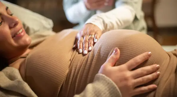 Manos sobre el vientre de una mujer embarazada, quizás consultando una tabla de contracciones de parto.