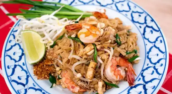 En tallrik med pad thai med räkor, böngroddar, lime och gröna lökar. En klassisk thailändsk rätt.