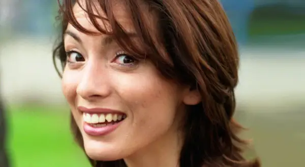 Close-up of a young woman with brown hair, smiling and looking to the side.