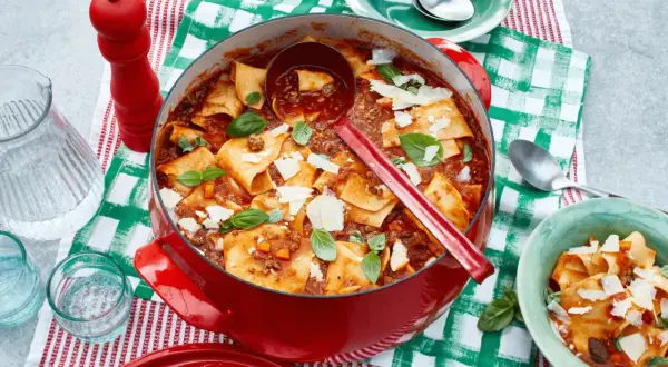 Herzhafte One Pot Lasagne in rotem Gusseisentopf, garniert mit Basilikum und Parmesan. Einfach und lecker!
