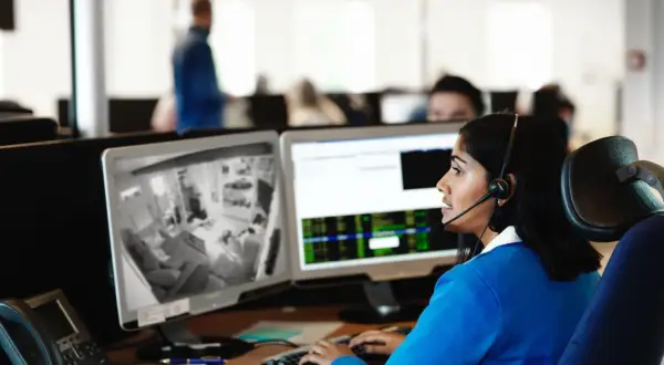 Kvinna med headset övervakar kameror på en arbetsplats, följer brandrutiner.